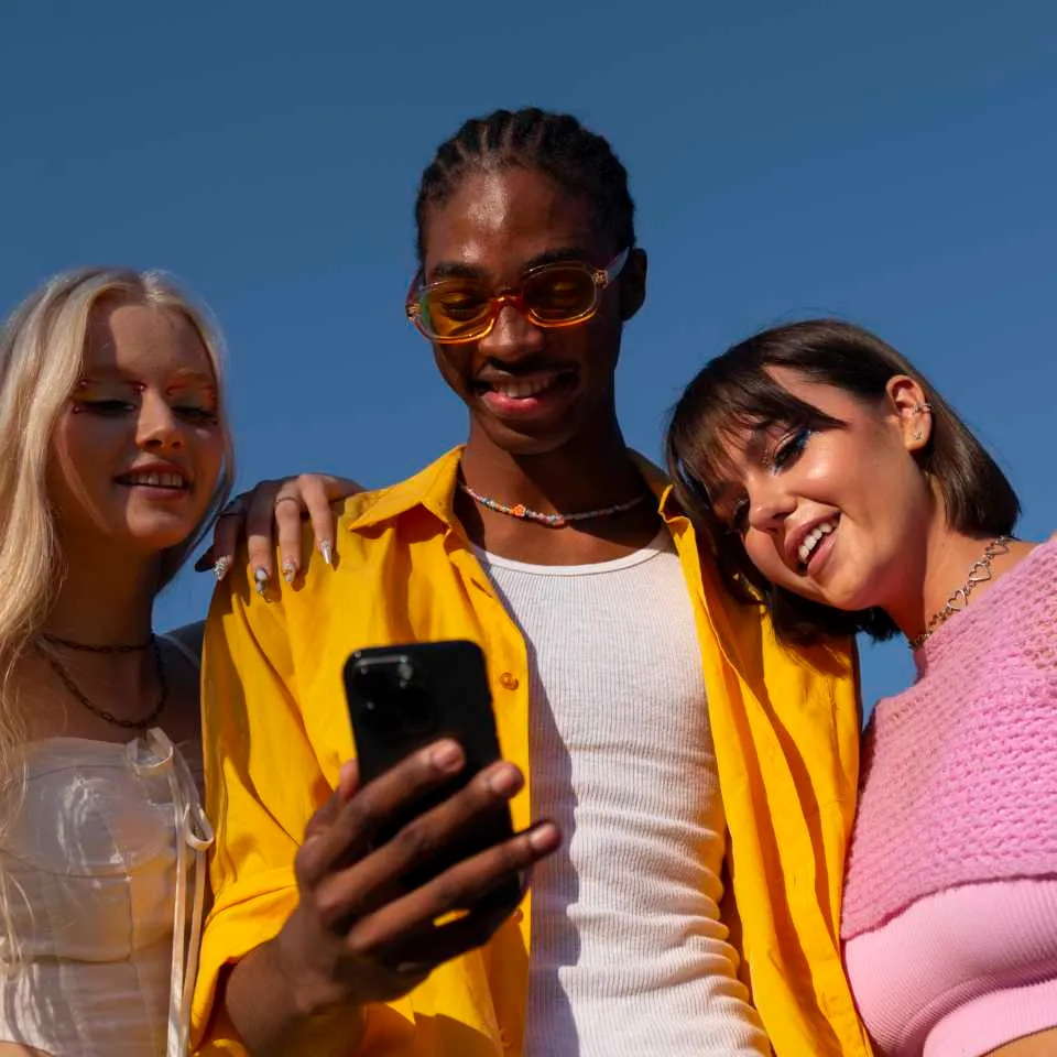 Three young friends in colourful clothes looking at a phone together against a blue sky