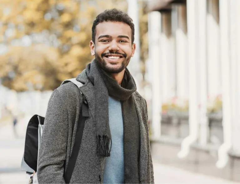 Smiling young man with a backpack and scarf on a street in autumn light