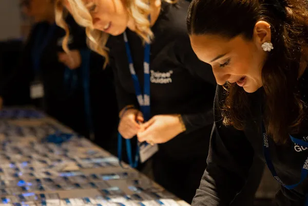 Two hosts in TraineeGuiden tops and lanyards laying out name badges on a table at TraineeDagen
